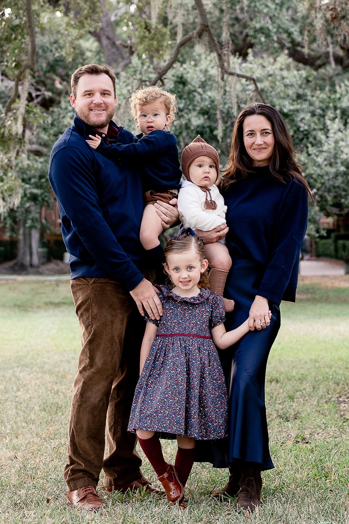 Family of four standing in a park with trees and greenery in the background